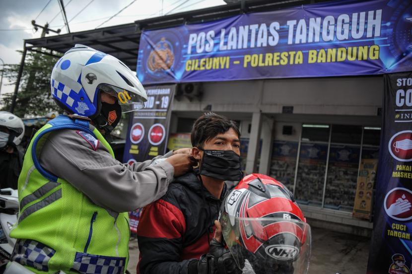 Petugas kepolisian memakaikan masker kepada seorang pengendara saat operasi kepatuhan memakai masker di Posko Lantas Tangguh, Cileunyi, Kabupaten Bandung, Jawa Barat, Rabu (10/2/2021). Kegiatan tersebut terkait pelaksanaan PPKM berskala mikro yang merupakan perpanjangan dari PPKM Jawa-Bali guna mendorong Kabupaten Bandung menjadi zona hijau COVID-19, yang digelar hingga 26 Februari 2021.