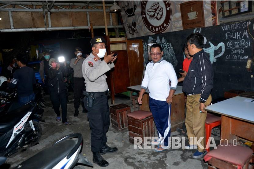 Petugas kepolisian membubarkan warga yang berkumpul di salah satu waruNg kopi 