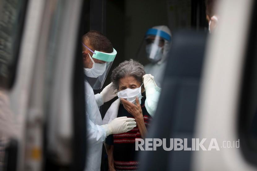 Petugas kesehatan memakaikan masker untuk wanita lanjut usia ketika dia dievakuasi dari panti jompo. Brasil dan Meksiko menyumbang dua pertiga dari jumlah kematian Covid-19. Ilustrasi.