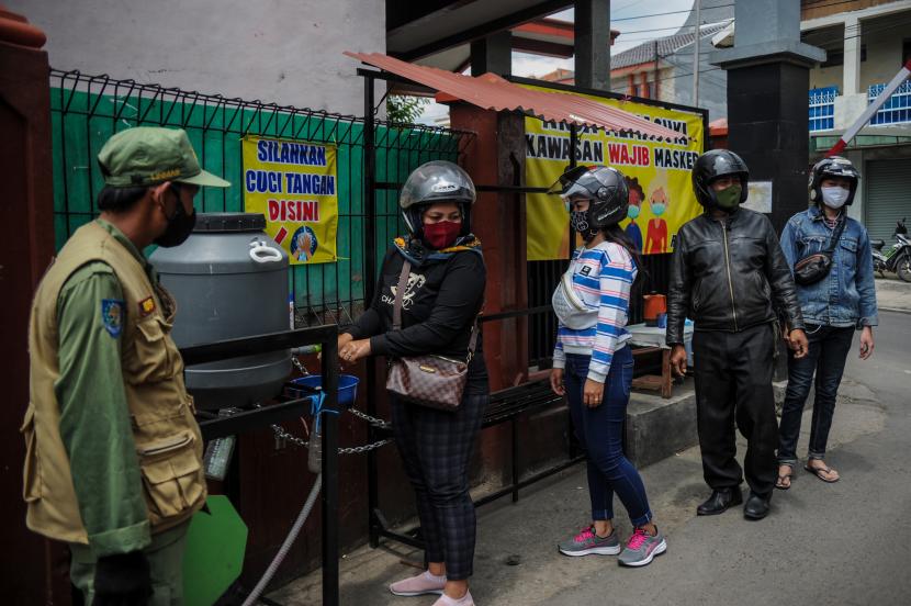Petugas Linmas mengawasi warga yang mencuci tangannya sebelum memasuki wilayahyang menerapkan mini lockdown atau Pembatasan Sosial Berskala Mikro (PSBM) di tingkat RW dan kelurahan selama 14 hari ke depan. 