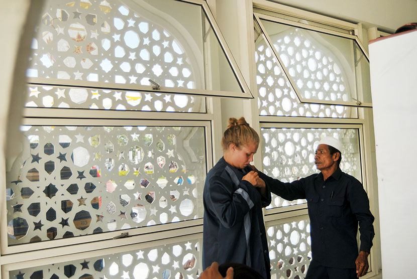 Petugas masjid membantu mengenakan baju khusus penutup aurat kepada wisatawan asing non muslim yang berkunjung di Masjid Raya Baiturrahman, Banda Aceh, Minggu (15/4). 