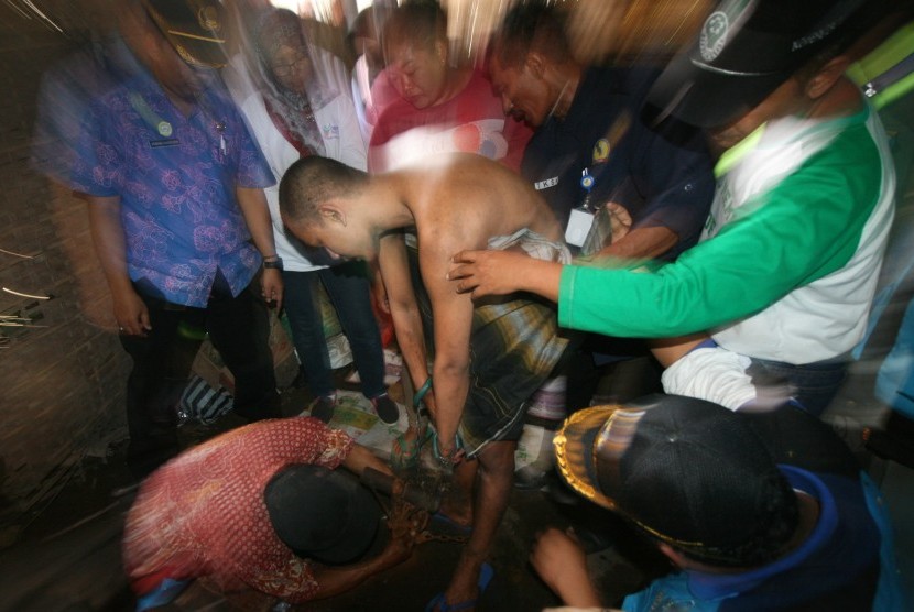 Petugas melepaskan rantai yang mengikat tangan dan kaki penderita gangguan jiwa berinisial FN usai dilepaskan dari pasungan di Desa Pehwetan, Kediri, Jawa Timur, Rabu (5/4).