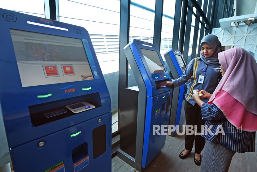 Petugas memandu warga melakukan transaksi pembelian tiket penyeberangan di anjungan tiket mandiri di Pelabuhan Merak, di Cilegon, Banten, Jumat (20/12/2019). 