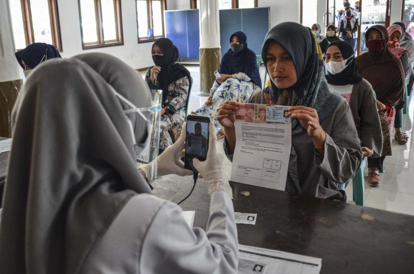 Petugas memotret identitas penerima bantuan sebagai tanda bukti saat penyaluran bantuan sosial (bansos) di Kantor Desa Sindangherang, Kabupaten Ciamis, Jawa Barat.
