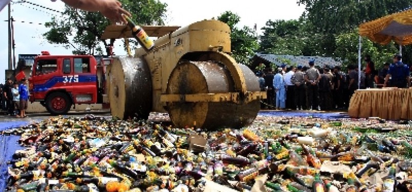 Petugas menggunakan alat berat memusnahkan ribuan botol minuman keras (miras). 