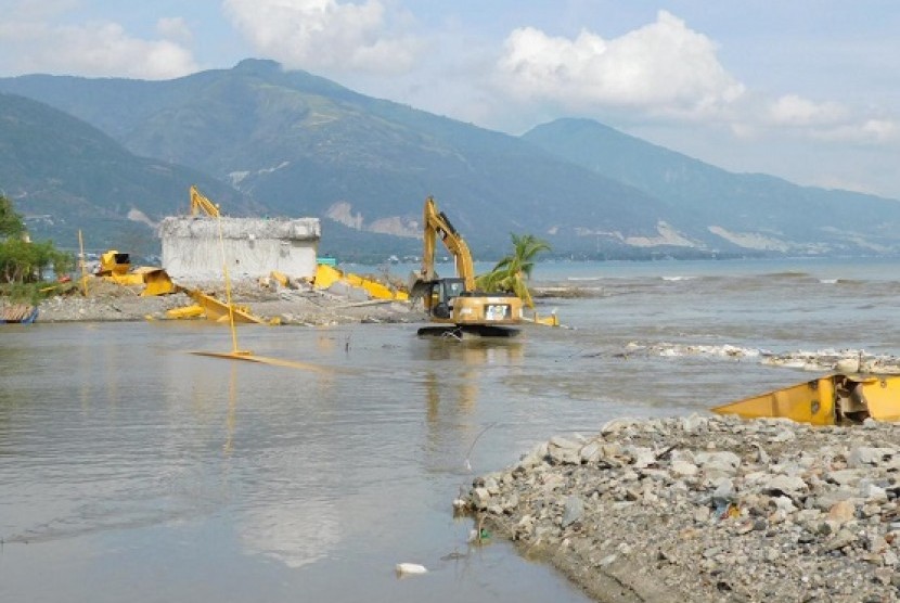 Petugas menggunakan alat berat untuk meratakan sisa reruntuhan puing Jembatan Palu IV atau jembatan kuning , di Palu Kamis (8/11)