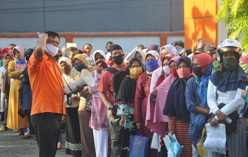 Petugas mengingatkan warga agar menjaga jarak saat mengantre penyaluran bansos tunai Kemensos, di Kantor Pos Khatib Sulaiman, Padang, Sumatera Barat, Jumat (15/5/2020). Sebagian besar warga tidak mengikuti protokol pencegahan COVID-19 dengan mengantre tanpa jaga jarak.