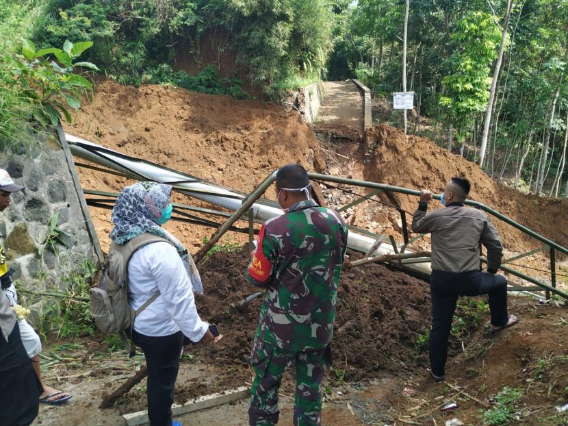 Petugas menunjukan jembatan yang terputus tertimpa lonhsor di Desa Bugel, Kecamatan Ciawi, Kabupaten Tasikmalaya, Rabu (10/7). 