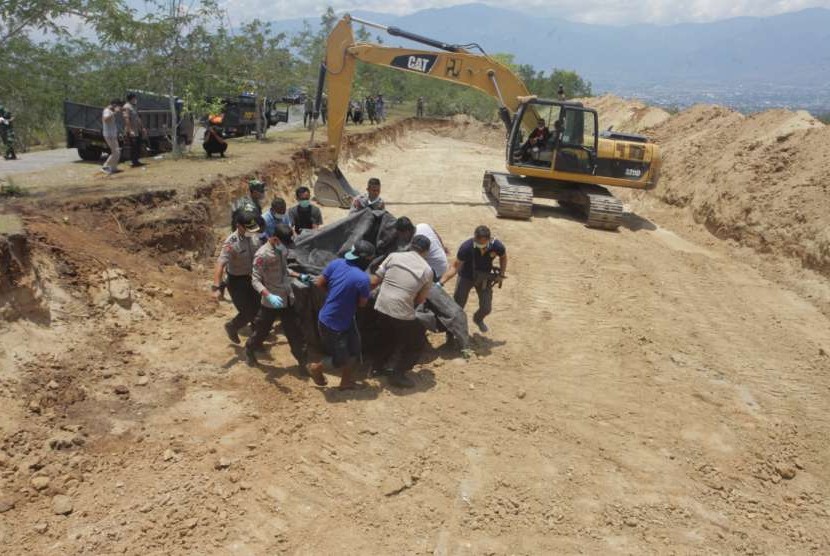 Petugas menurunkan jenazah korban gempa tsunami Palu untuk dimakamkan di Poboya, Mantikulore, Palu, Senin (1/10).