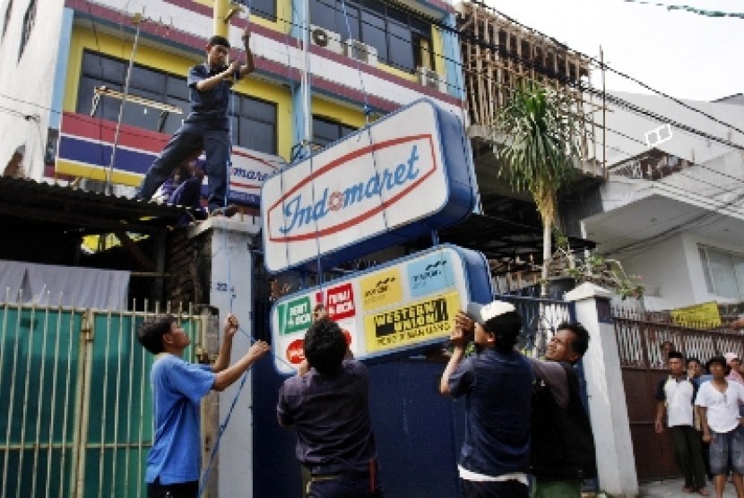 Petugas menurunkan papan reklame saat penertiban minimarket di Indomaret, Jalan Keagungan, Jakarta, Kamis (26/5). 