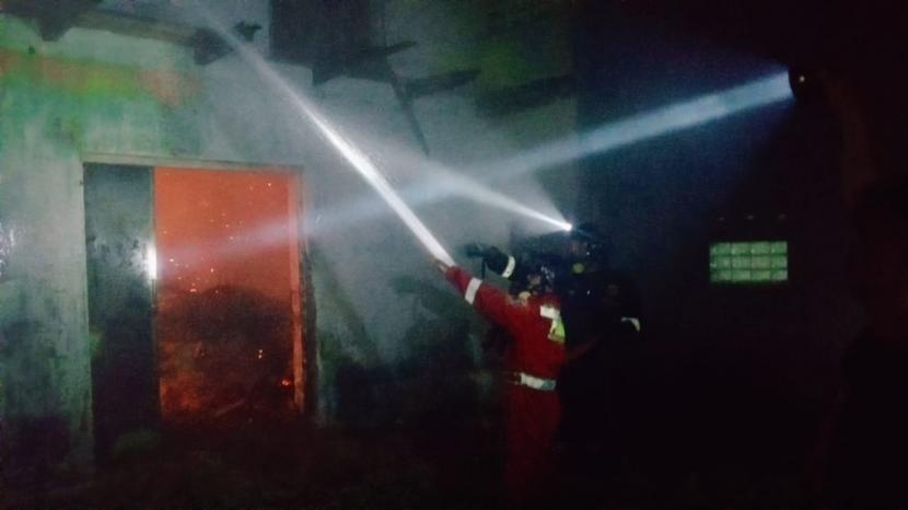 Petugas menyemprotkan air ke arah gudang penyimpanan kayu yang terbakar di Kabupaten Kuningan, Sabtu (10)12/2022) malam. 
