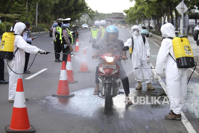 Petugas menyemprotkan disigektan kepada pengemudi sepeda motor di Kota Surabaya, Jawa Timur, Ahad (22/3).