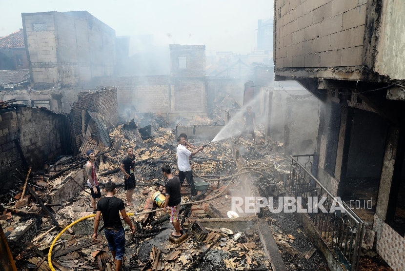 Petugas pemadam kebakaran dibantu warga memadamkan sisa api yang membakar permukiman di pinggiran rel kereta api kawasan Pesing Koneng, Kebon Jeruk, Jakarta Barat, Kamis (10/3). (Republika/Yasin Habibi)