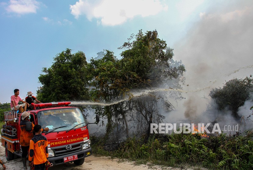 Petugas Pemadam Kebakaran Kota Pekanbaru bersama BPBD Pekanbaru menyemprotkan air saat memadamkan kebakaran lahan gambut di Pekanbaru, Riau, Jumat (2/8/2019). 