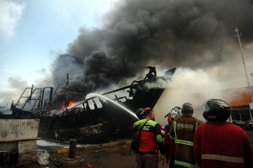 Petugas pemadam kebakaran menyemprotkan air pada kapal nelayan yang terbakar di Pelabuhan Tegal, Jawa Tengah, Sabtu (29/1/2022). Sebanyak 13 kapal nelayan yang akan melaut terbakar sekitar pukul 04.30 WIB dan pihak terkait masih menyelidiki penyebab musibah tersebut. 