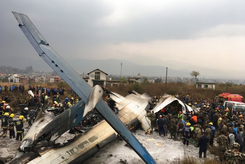 Petugas penyelamat berdiri di puing pesawat asal Bangladesh yang terbakar di bandara Nepal, Senin (12/3).