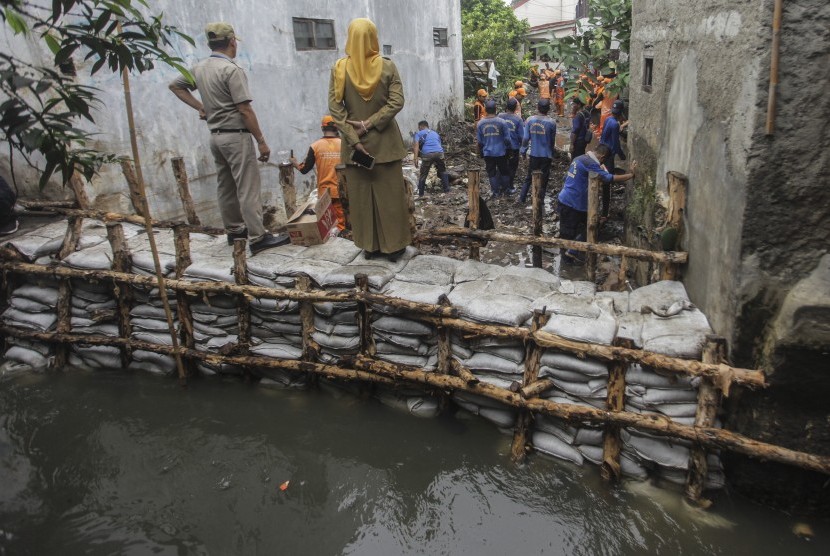 Petugas PPSU membersihkan lumpur yang menggenangi jalan pemukiman warga karena tanggul aliran Kali Pulo jebol di Kelurahan Jati Padang, Kecamatan Pasar Minggu, Jakarta, Senin (14/1/2019).