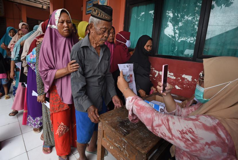 Petugas PT POS (kanan) memotret warga penerima manfaat saat penyaluran bantuan sosial tunai (BST) untuk keluarga terdampak pandemi di halaman SD Negeri Kilasah, di Kasemen, Serang, Banten, Sabtu (13/2/2021). Dinsos Provinsi Banten mencatat terdapat 315.250 KK akan mendapat BST mulai Januari hingga April 2021 sebesar Rp300 ribu per-KK perbulan.