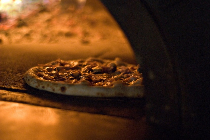 Pizza dibakar dalam oven dengan kayu bakar.