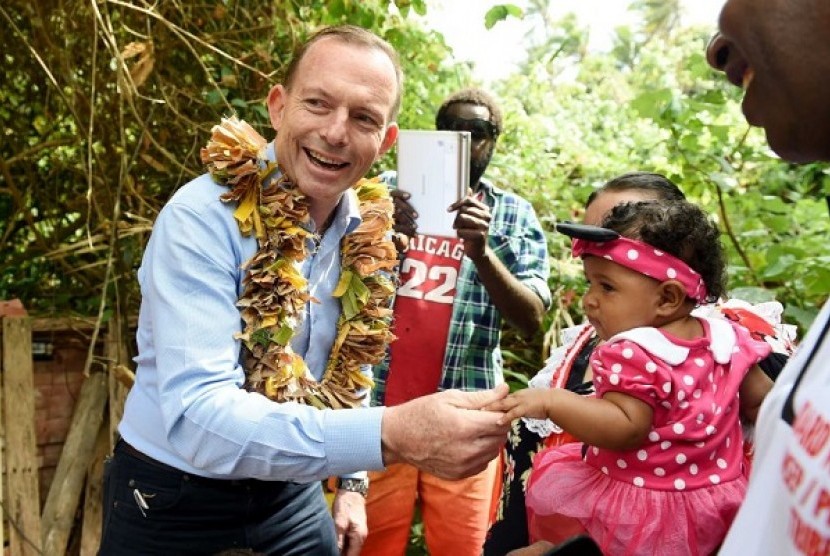 PM Abbott memegang tangan seorang bayi ketika berkunjung ke makam pegiatn pertahanan aborijin Eddie Mabo di Mer Island hari Senin. (AAP: Tracey Nearmy)