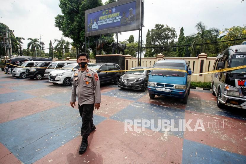 Polisi melintas di depan barang bukti kendaraan travel gelap di Polres Bogor, Cibinong, Kabupaten Bogor, Jawa Barat, Rabu (5/5/2021). Sat Lantas Polres Bogor berhasil menangkap dan menyita sebanyak sembilan kendaraan travel gelap yang beroperasi di wilayah Kabupaten Bogor yang menyalahgunakan trayek atau jalan yang dilalui untuk mengantarkan para pemudik sesuai lokasi tujuan pemudik. 