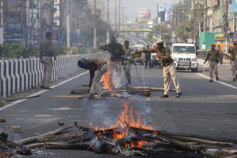 Polisi membersihkan kayu yang dibakar di tengah jalan oleh pendemo di Gauhati, India, Kamis (12/12). Polisi menahan puluhan orang dan menerapkan jam malam di sejumlah distrik di Assam. India meloloskan RUU Amandemen Kewarganegaraan yang dinilai diskriminatif terhadap Muslim.