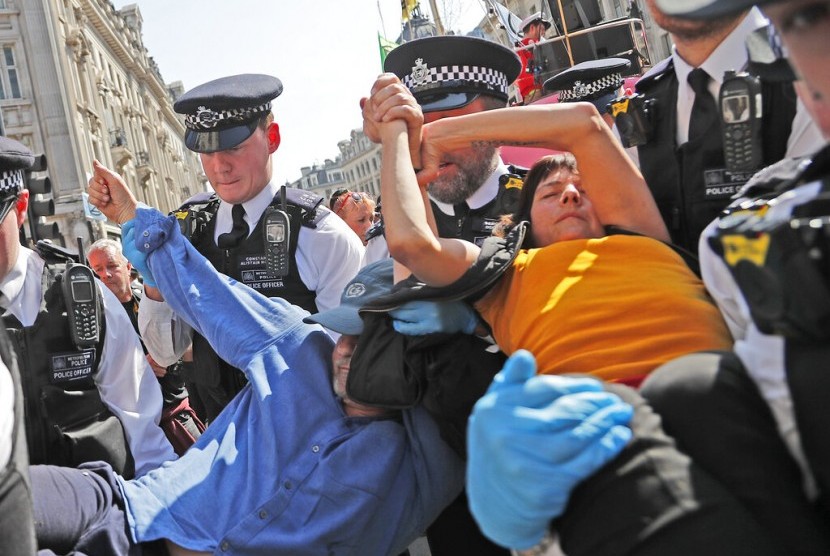 Polisi menahan pasangan pemrotes perubahan iklim yang mengelem tangan mereka di Oxford Circus di London, Jumat (19/4). 