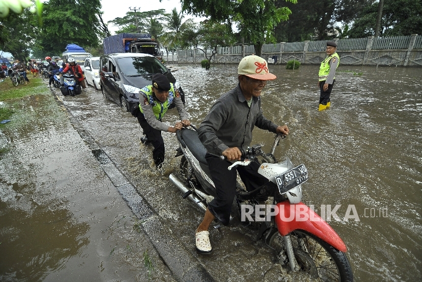   Polisi mendorong pengguna kendaraan bermotor berusaha melintasi banjir di kawasan Jalan Raya Rancaekek di depan Pabrik PT Kahatek, Kabupaten Bandung, Jawa Barat, Selasa (1/11).(Republika/Mahmud Muhyidin)