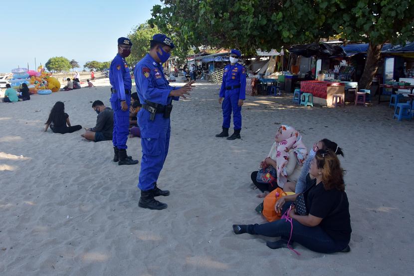Polisi menegur wisatawan yang tidak menggunakan masker di Pantai Sanur, Bali.