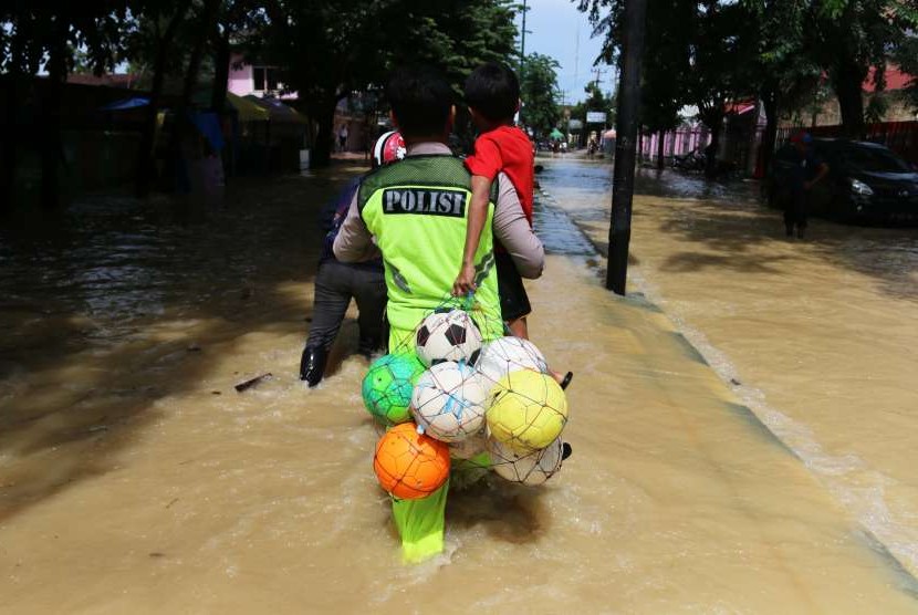 Polisi menggendong seorang anak melintasi banjir di Medan
