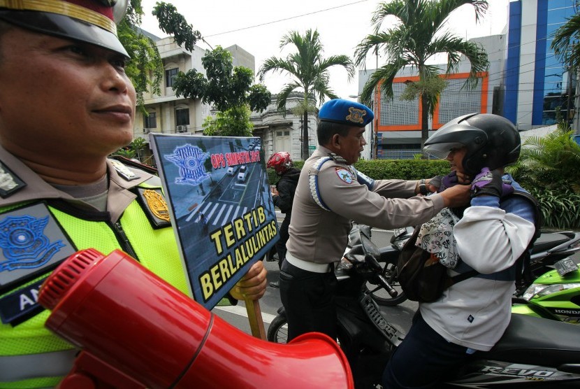 Polisi mengikat tali pengaman helm milik pengendara motor yang tidak terpasang saat Operasi Simpatik (ilustrasi)