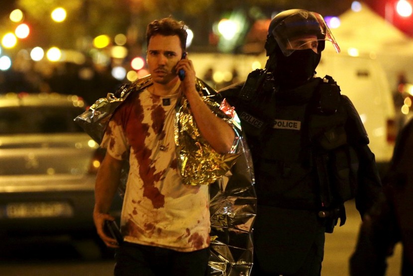 Polisi Prancis menolong seorang korban selamat aksi penembakan di Bataclan Concert Hall, Paris, Jumat (13/11). Laporan terkini menyebut 140 orang tewas akibat insiden ini.
