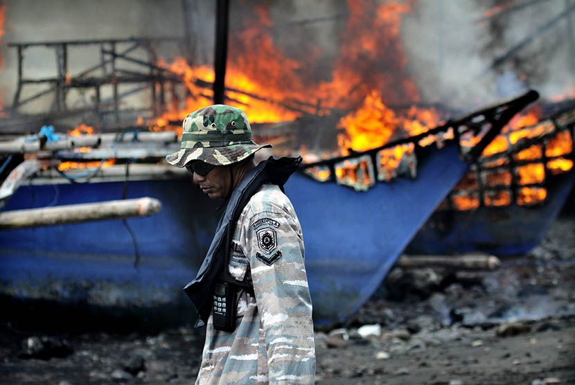 Prajurit TNI AL berjalan di samping kapal penangkap ikan ilegal berbendara negara asing yang dibakar di Pangkalan Angkatan Laut (Lanal) Kota Tahuna, Kepulauan Sangihe, Sulawesi Utara, Kamis (31/12).  (Antara/Stenly Pontolawokang)