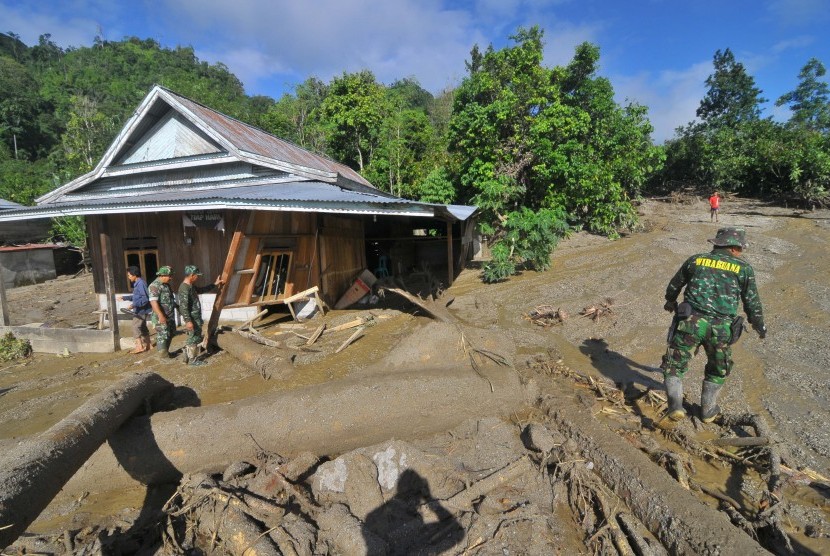 Prajurit TNI menyaksikan rumah yang rusak akibat banjir bandang 