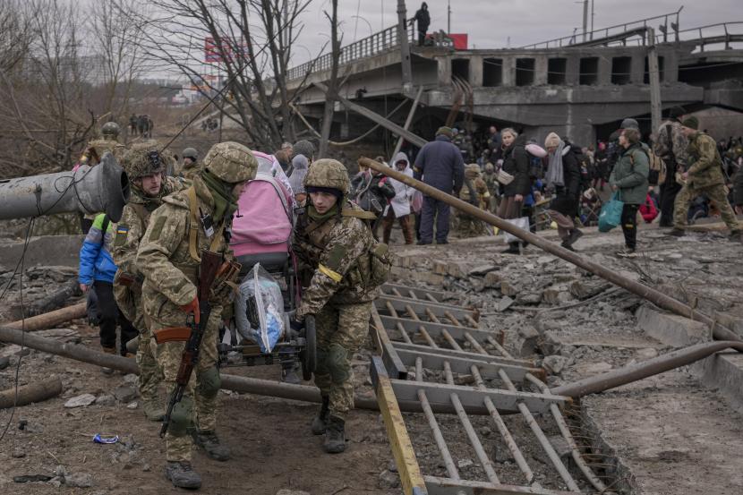 Prajurit Ukraina membawa kereta bayi setelah menyeberangi sungai Irpin di jalur improvisasi di bawah jembatan yang dihancurkan oleh serangan udara Rusia, sambil membantu orang-orang yang melarikan diri dari kota Irpin, Ukraina, Sabtu, 5 Maret 2022.