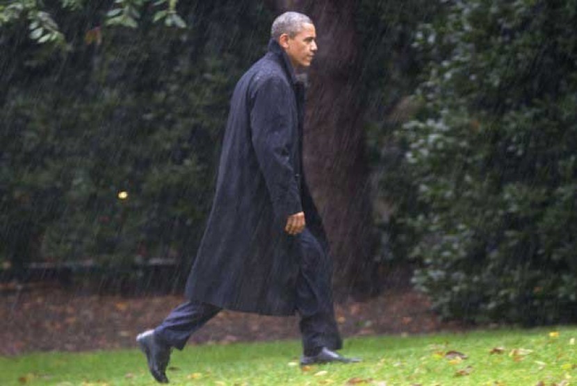  Presiden Barack Obama di tengah hujan deras berjalan menuju Gedung Putih di Washington, Senin (29/10) waktu setempat.  (Jacquelyn Martin/AP)