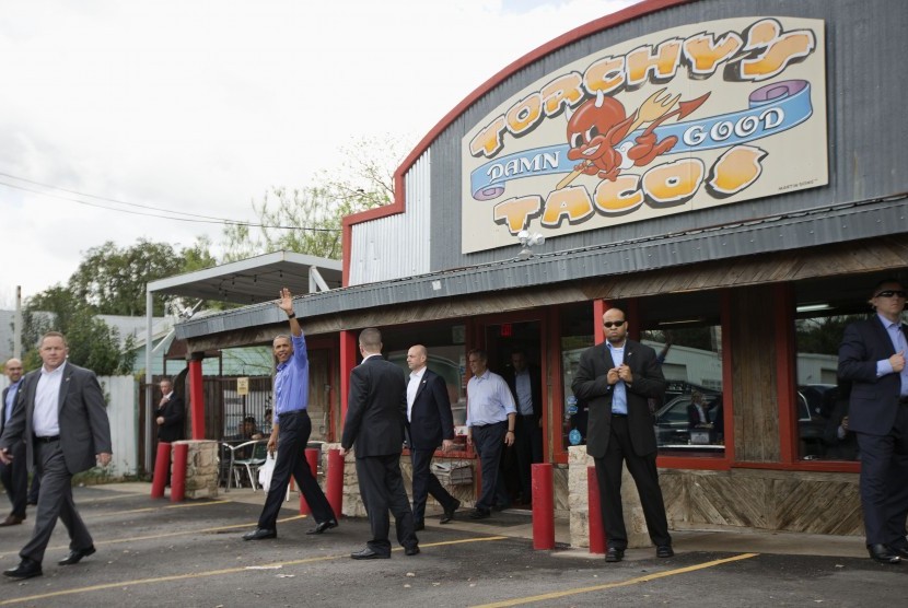 Presiden Barack Obama melambaikan tangan usai keluar dari kedai taco sambil menenteng pesanan makanannya, Jumat (11/3), di Texas.