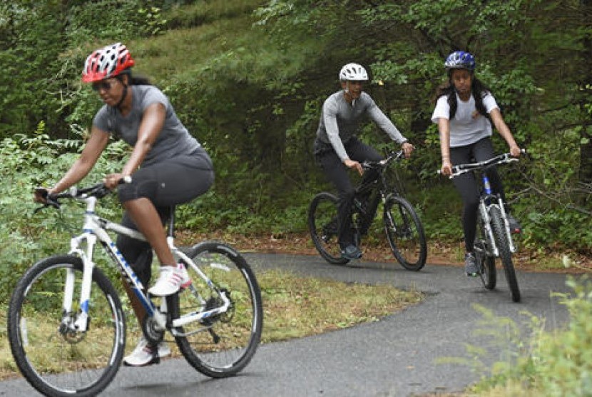 Presiden Barack Obama, putrinya Malia dan Ibu Negara Michelle Obama (kiri) saat bersepeda di West Tisbury, Massachussets di Martha's Vineyard.