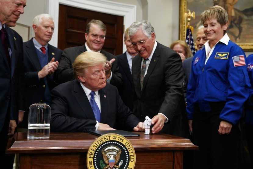 Presiden Donald Trump memegang patung kecil yang diberikan mantan astronot Jack Scmitt (kanan), setelah menandatangani kebijakan mengirim astronot kembali ke Bulan dan Mars, Senin (11/12).