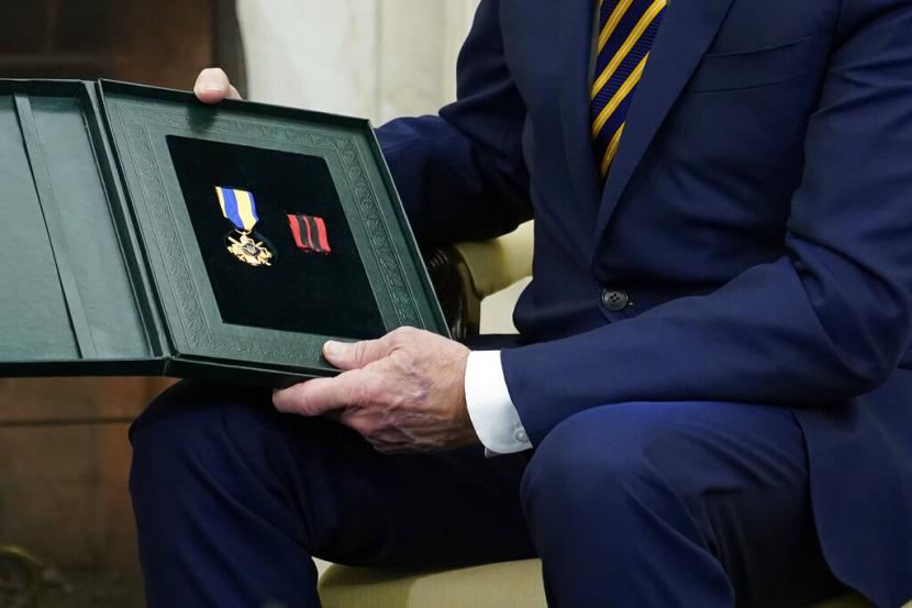 Presiden Joe Biden memegang hadiah yang dia terima dari Presiden Ukraina Volodymyr Zelenskyy saat mereka bertemu di Oval Office Gedung Putih, Rabu, 21 Desember 2022, di Washington.