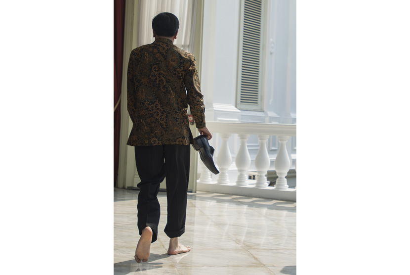 Presiden Joko Widodo berjalan sambil membawa sepasang sepatunya usai mencetak tapak tangan dan kakinya di Teras Belakang Istana Merdeka, Jakarta, Selasa (13/10). 