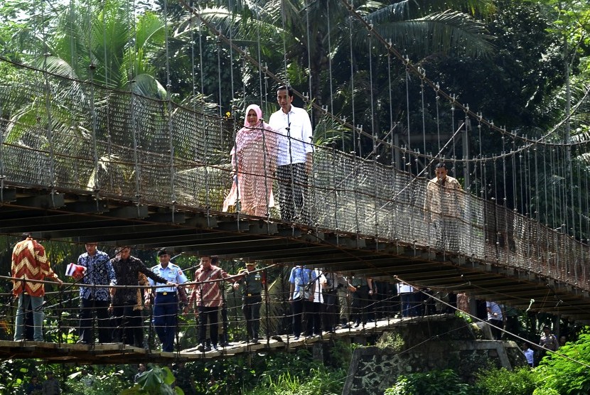 Presiden Joko Widodo bersama Ny Iriana Jokowi melewati jembatan gantung seusai membagikan sembako dan uang kepada warga kurang mampu di Kampung Ranca Garut, Sangiang Tanjung, Lebak, Banten, Senin (4/7). 