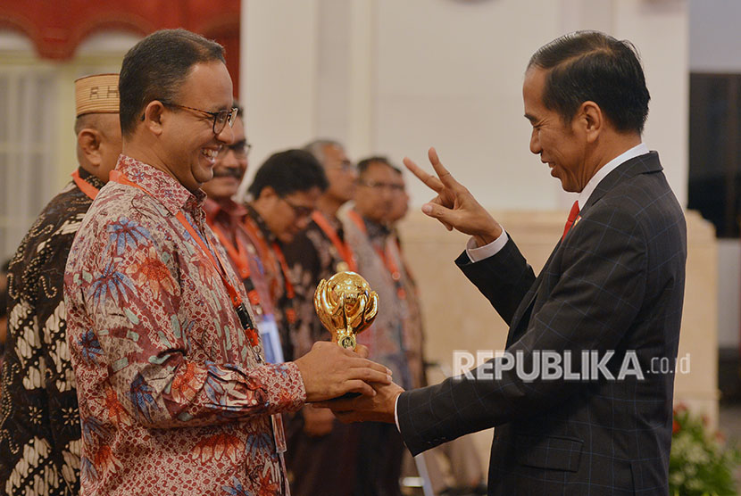 Presiden Joko Widodo (kanan) menyerahkan penghargaan Jaminan Kesehatan Nasional-Kartu Indonesia Sehat (JKN-KIS) Award kepada Gubernur DKI Jakarta Anies Baswedan ketika menerima pengguna manfaat kartu tersebut di Istana Negara, Jakarta, Rabu (23/5). 