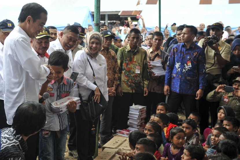 Presiden Joko Widodo (kiri) didampingi Menteri Kesehatan Nila F. Moeloek (kelima kiri) memberikan buku kepada anak-anak korban gempa di halaman Masjid Atta Darut, Pidie Jaya, Aceh, Jumat (9/12).