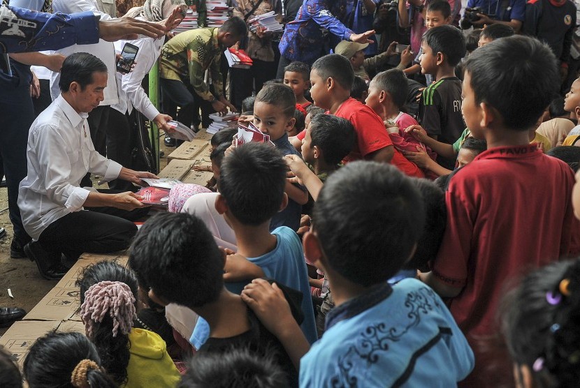 Presiden Joko Widodo (kiri) memberikan buku kepada anak-anak korban gempa di halaman Masjid Atta Darut, Pidie Jaya, Aceh, Jumat (9/12).