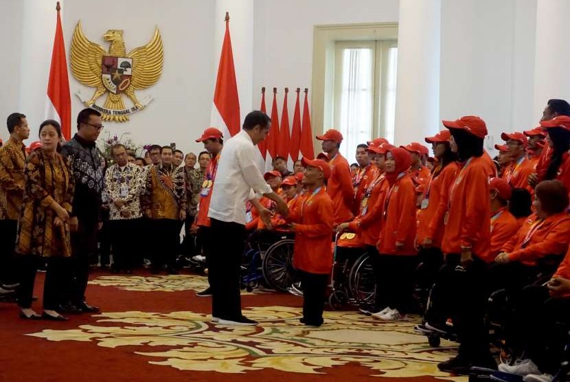Presiden Joko Widodo (tengah) menyerahkan bonus prestasi kepada peraih perak dari cabang olahraga renang Asian Para Games 2018, Aris, sebagai perwakilan atlet, di Istana Kepresidenan Bogor, Jawa Barat, Sabtu (13/10).