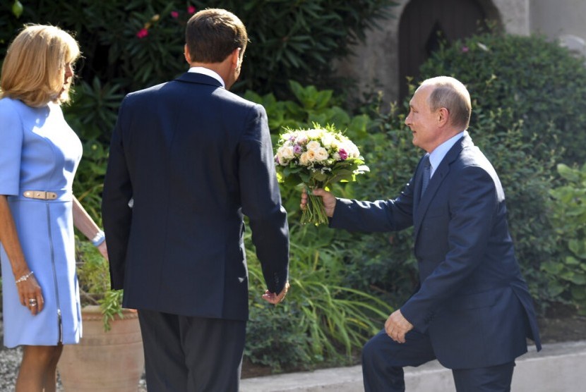 Presiden Rusia Vladimir Putin (kanan) membawa sebuah buket bunga mawar untuk Ibu Negara Prancis Brigitte Macron di Benteng Fort de Bregancon di Bormes-les-Mimosas, selatan Prancis, Senin (19/8). Tampak Presiden Prancis Emmanuel Macron menghadap belakang.