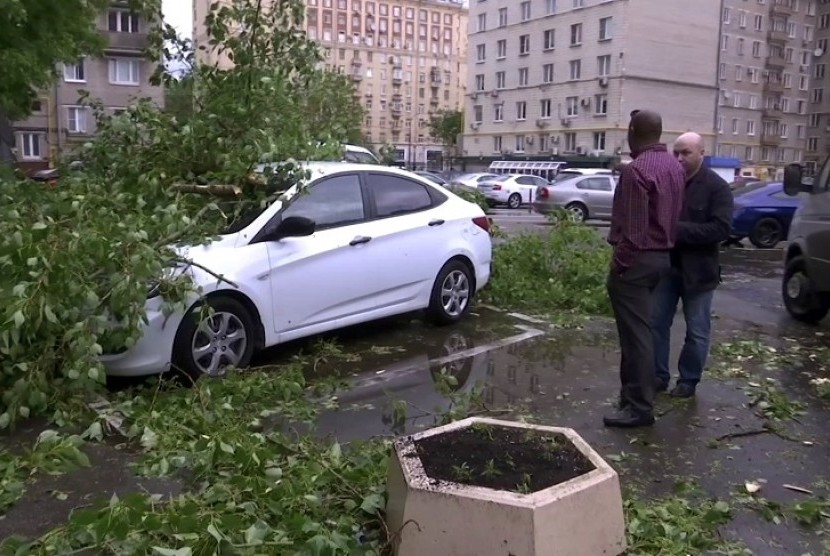 Pria berdiri di dekat kendaraan yang hancur tertimpa pohon yang tumbang, di area perumahan di Moskow, Russia, Senin, 29 Mei waktu setempat. Badai petir dan angin kencang melanda Moskow dan sekitarnya pada hari Senin, menewaskan 11 orang dan melukai puluhan lainnya. 