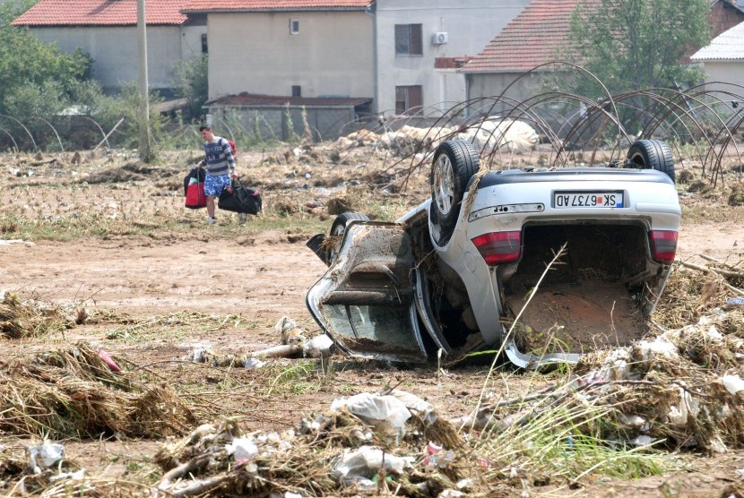 Pria berjalan dekat mobil yang terbalik akibat banjir di kota Cento, dekat Skopje, Macedonia.