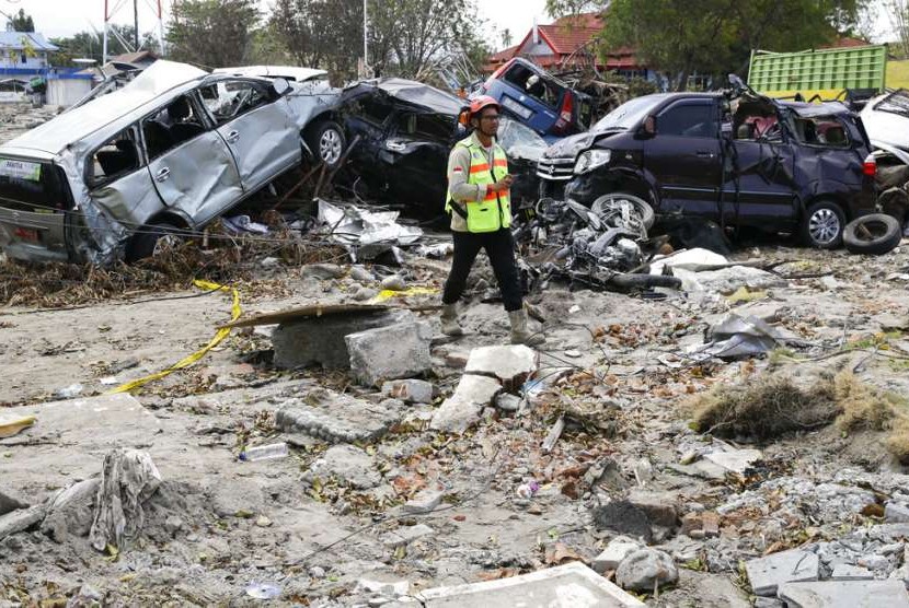 Pria berjalan di puing-puing mobil yang rusak akibat gempa dan tsunami di Kota Palu, Sulteng, Kamis (4/10).